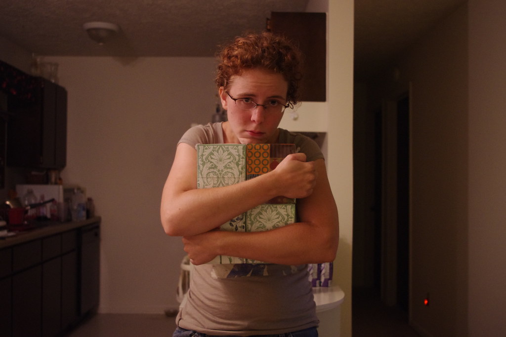 A woman with curly hair and glasses looking at the camera while tightly clutching several patterned boxes to her chest.