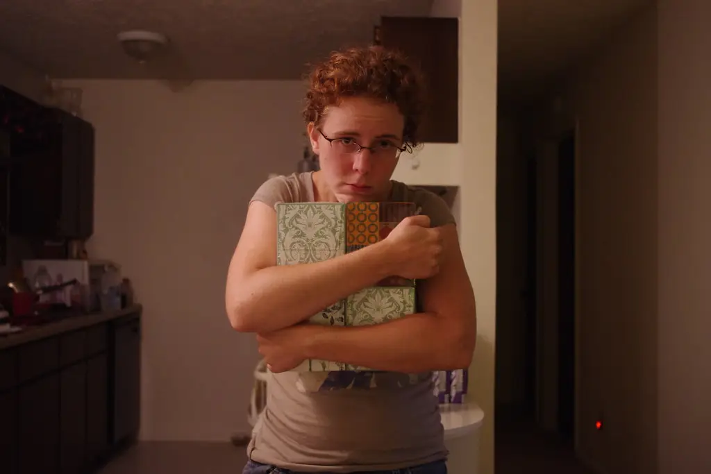 A woman with curly hair and glasses looking at the camera while tightly clutching several patterned boxes to her chest.